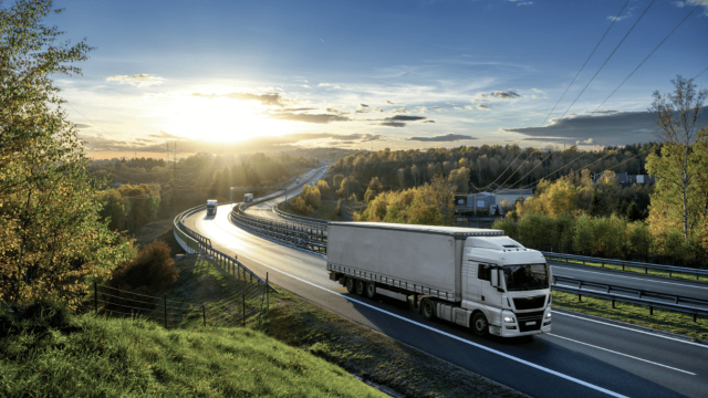 Truck on the highway in sunset with green trees on both side of the road